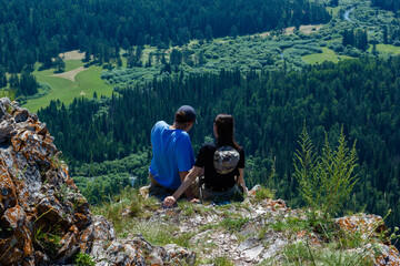 A young guy and a girl are sitting on a rock against the background of a river valley