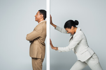 angry african american businesswoman screaming and pulling wall near smiling businessman on grey - obrazy, fototapety, plakaty