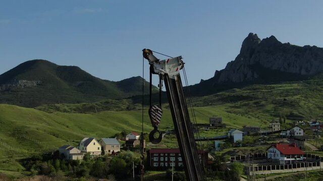 Main boom head of building mobile crane at the background of rural Buildings. After hoses with mountains the background changing into the blue sky.