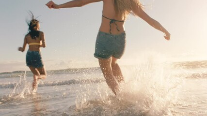 two women on beach splashing sea water at each other having fun teenage girls playing game on warm summer day by the ocean enjoying summertime holiday vacation