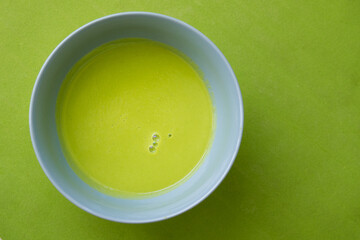 Velvety pea soup in a bowl on green surface, top view, selective focus, green tone on tone.