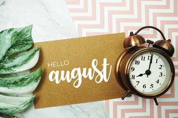 Hello August typography text on paper card with alarm clock and Monstera leave
