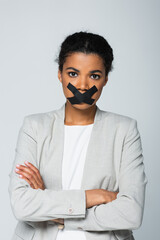 african american businesswoman with scotch tape on mouth standing with crossed arms isolated on grey