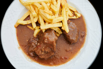 Braised pork cheeks in brown red wine sauce with french fries on a classic design white plate