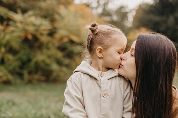 Young happy and smiling mom with her little daughter in arms hugging and kissing spending a weekend on a walk in autumn park. selective focus, noise effect, Autumnal mood