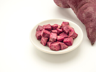 Top view of purple yams whole with diced yams in a bowl isolated on white background. Purple sweet potatoes. Vegan fruit and healthy fruits concept