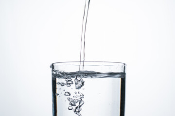 Jet of water or alcohol is pouring into a glass with splashes and bubbles, copy space