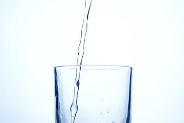 Jet of water or alcohol is pouring into a glass with splashes and bubbles, copy space