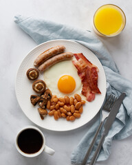 Delicious english breakfast. Tasty mushrooms, fried egg yolks, kidney beans, grilled sausages, smoky bacon, fresh orange juice, hot cup of coffee. Ketogenic meal on white background