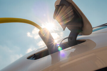 Woman plugging in electric car charger against sun and blue sky.