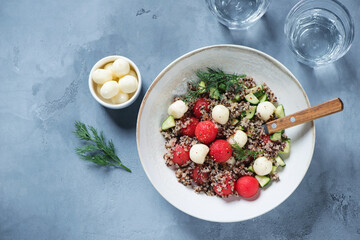 Salad with quinoa, watermelon balls, cucumber and scamorza cheese, flatlay over grey concrete...