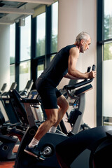 Fototapeta na wymiar Mature athletic man during sports training on stationary bike in gym.