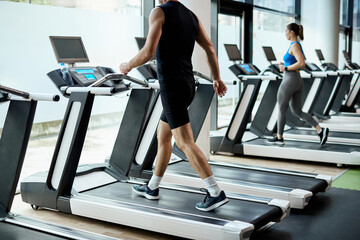 Fototapeta na wymiar Unrecognizable athlete walks on treadmill while warming up for gym workout.