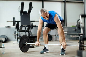 Mature sportsman exercises strength with barbell during gym workout.