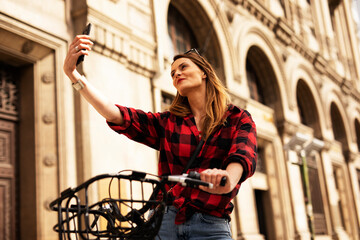 Young blonde woman on bicycle on the street. Beautiful girl taking selfie photo.