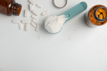 Measuring scoop of amino acids powder and pills on white table, flat lay. Space for text