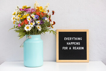 Everything happens for a reason. Motivational quote on letter board and bouquet colorful flowers on white table against grey stone wall. Concept inspirational quote of the day