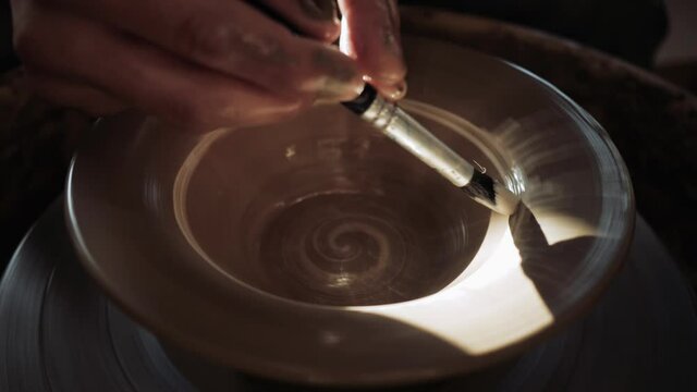 A potter paints a plate with white paint using a brush on a potter's wheel. High quality 4k footage