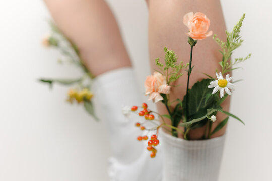A beautiful image on a white background with long slender legs in white stockings and autumn flowers and fashionable sports leather sneakers, perfect for a store catalog. flowers in socks.