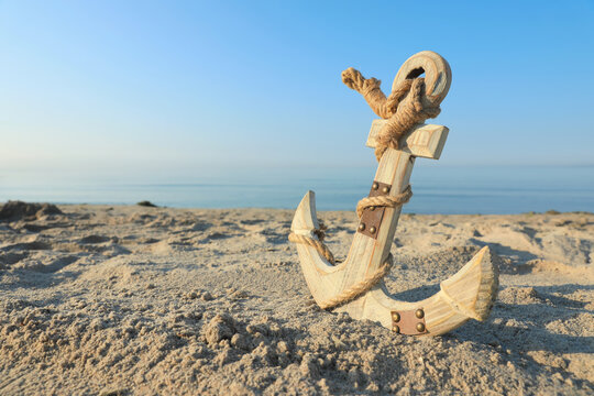 Wooden anchor with rope on sand near sea. Space for text