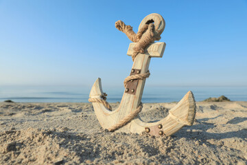 Wooden anchor with rope on sand near sea. Space for text