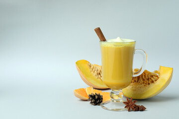 Glass of pumpkin latte and ingredients on light gray background