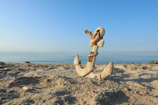 Wooden anchor with rope on sand near sea. Space for text