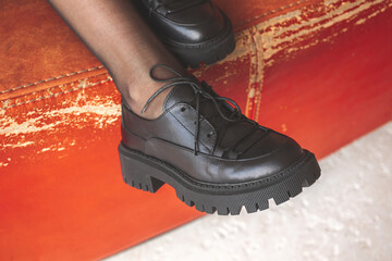 Woman legs in black sneakers or boots lying on old leather chair, young voyage background