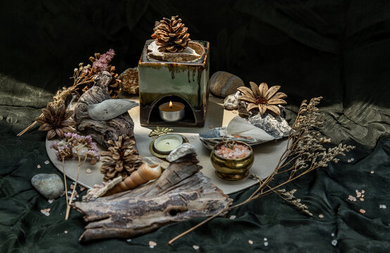 Beauty composition with Burning candle aroma oil lamp and Dry flower petals and Pine cones, Natural pine wood disc, Stones and Shells, Himalayan salt on dark background. Aromatherapy concept.