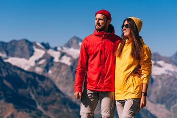 A traveling couple in hiking gear against the background of mountains. Two tourists on the top of...