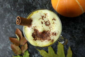 Glass of pumpkin latte, pumpkin and leaves on black smokey table