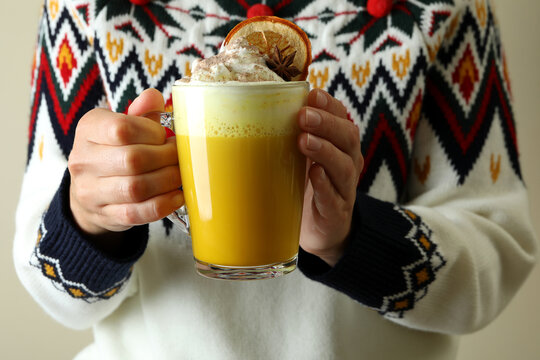 Woman in sweater holds glass of pumpkin latte