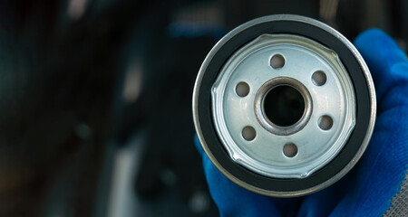 Replacing the oil filter. Car engine maintenance mechanic holds an oil filter in his hand against the background of an open car hood close up. Banner