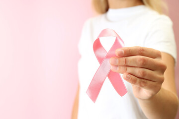 Young woman holds breast cancer awareness ribbon, close up