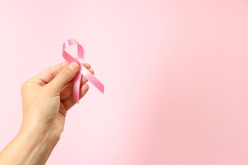 Female hand holds breast cancer awareness ribbon on pink background - obrazy, fototapety, plakaty
