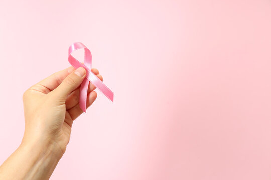 Female hand holds breast cancer awareness ribbon on pink background