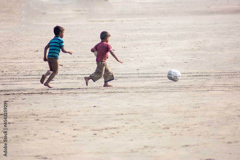 Poster closeup shot of two south asian boys running joyfully with a ball on a beach