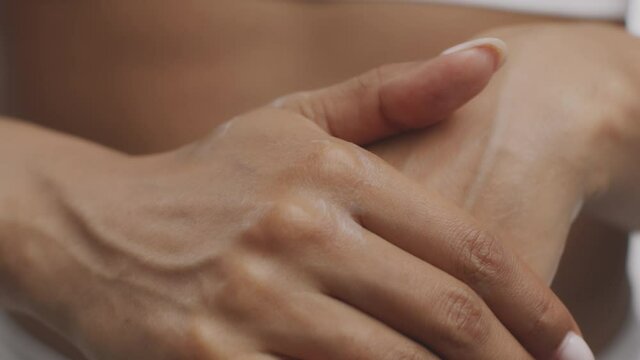 Skin pampering. Young woman applying moisturizing lotion on hands, massaging palms after caring procedures, slow motion