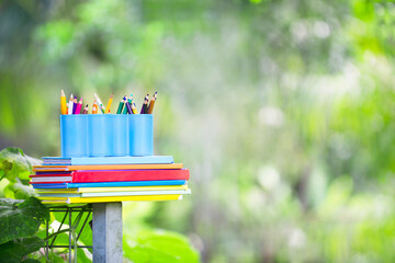 Colored pencils and books in outdoor.Stationeries with green leaves background.Homeschool and homeschooling objects.Study in park.Outdoor lesson.Education for elementary school concept.