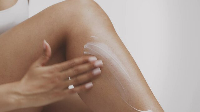 Body pampering after depilation. Close up of unrecognizable african american woman applying nourishing cream on leg s