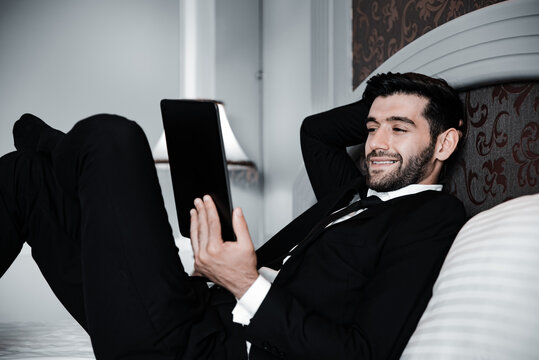 Handsome young bearded businessman lying on bed with tablet