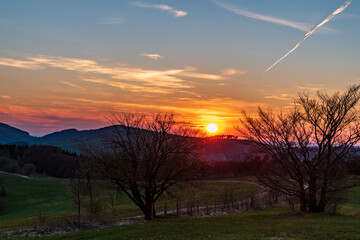 Sunset in mountains with hills, colorful sky, trees and meadows