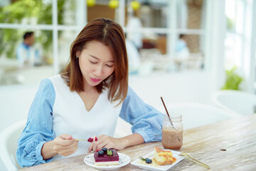 A beautiful Asian portrait is taking a spoonful of cakes on the table and eating them with happy eyes and expressions in the bakery.