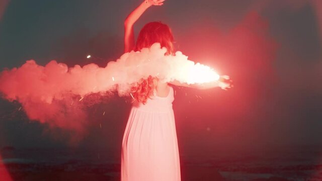 woman waving flare dancing on beach at dawn burning distress signal firework