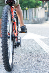 Fototapeta premium Close up of a child's legs mounted on his bicycle ready to start riding next to a white arrow sign painted on the ground indicating go ahead. Concept Keep going forward. High quality photo