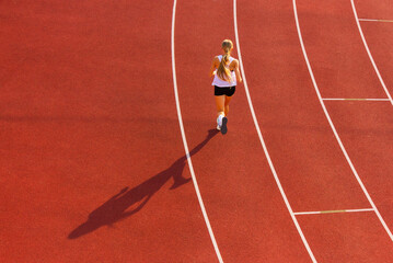 young woman in sportswear runs along the track of the stadium, back view. sports training and exercise. healthy lifestyle © x.marynka