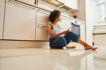 Curly-headed barefoot woman with the smartphone looking away