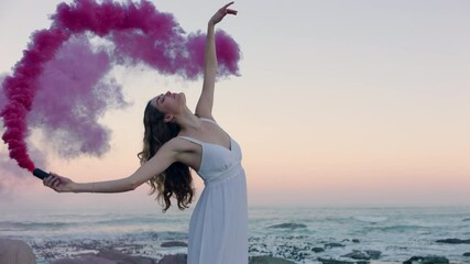 woman holding pink smoke bomb dancing on beach in early morning celebrating creative freedom