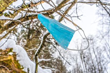 Blue surgical mask hanging in a tree at winter in forest. Coronavirus or Covid-19 topic.