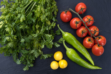 Vegetables ingredient parsley, cherry plum, hot pepper and cherry tomatoes on black Stone cutting board, recipe or dish. Top view flat